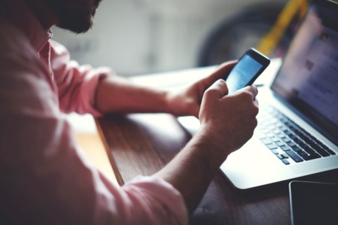 A person at a desk with a laptop and a smartphone in their hands.