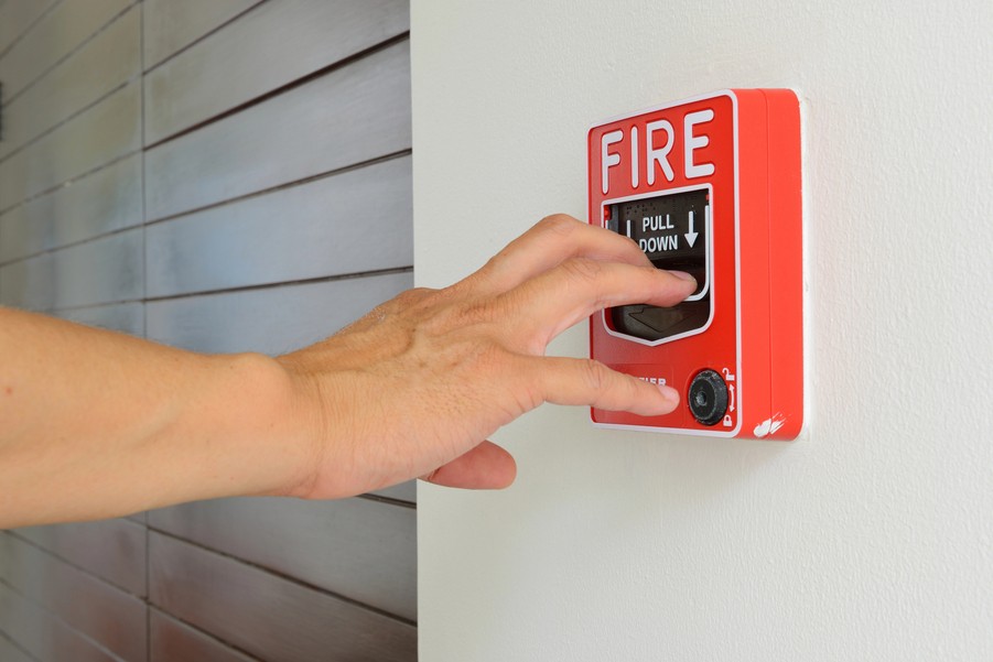 Hand pulling down a red fire alarm station on a wall for emergency activation.